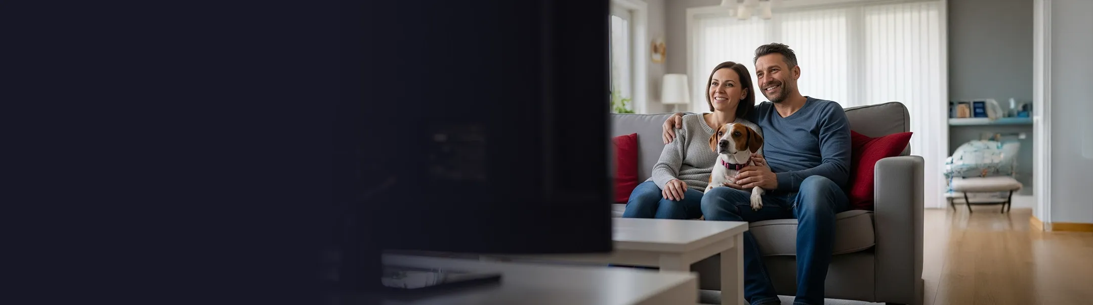 A couple watching TV while sitting on their couch with their dog